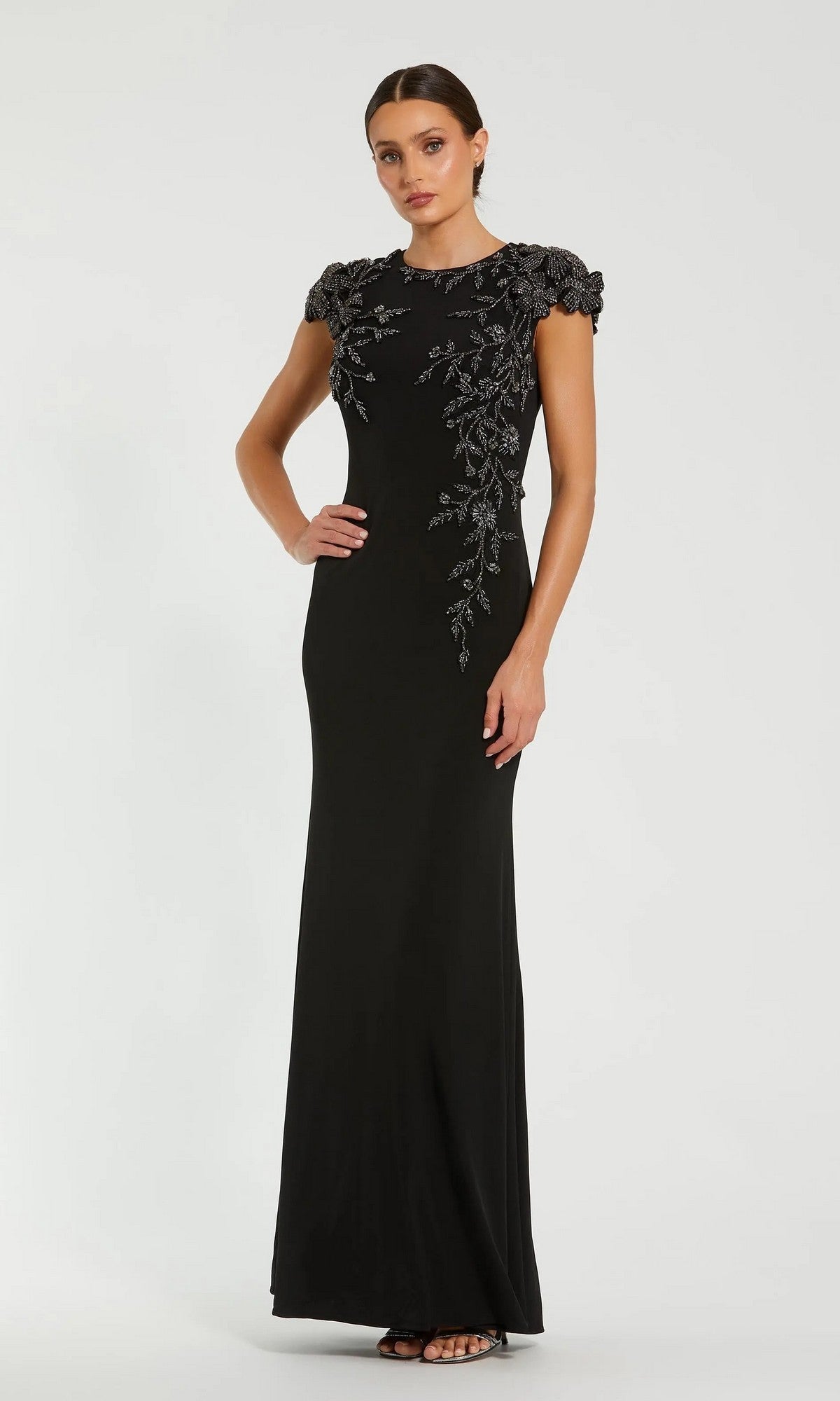 A woman models the Mac Duggal 11847 long formal dress in Black Multi, featuring short embellished sleeves and intricate silver floral embroidery on the bodice and shoulders for an elegant, beaded floral look.